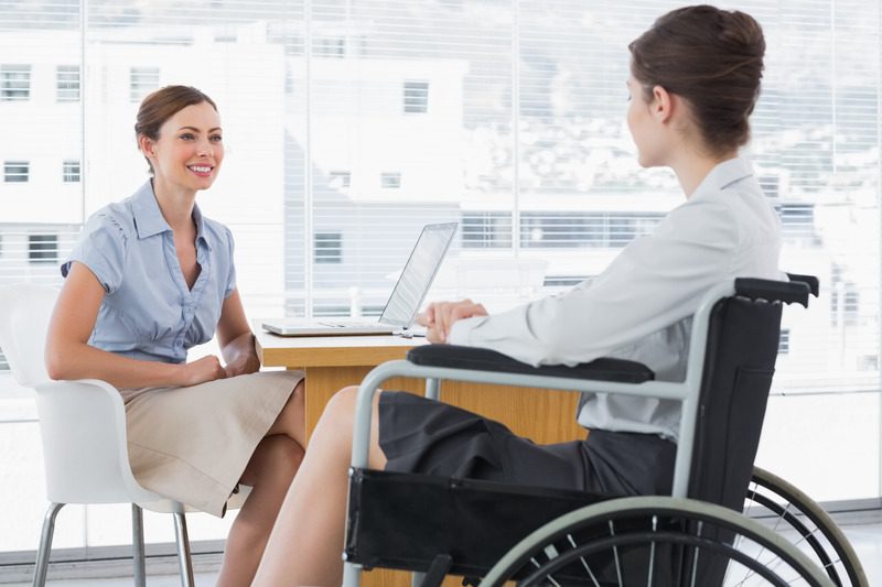 Businesswoman speaking with disabled colleague at desk in office